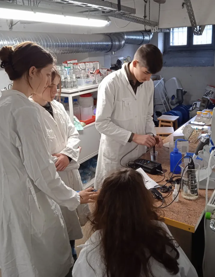 Uczniowie w fartuchach laboratoryjnych badają próbki wody w laboratorium