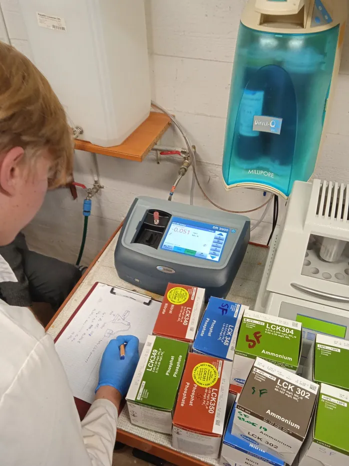 Uczeń w rękawiczkach notuje wyniki analizy wody przy fotometrze i zestawach testów chemicznych